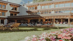 A two-story building with a covered patio area featuring wicker furniture and potted plants. - Ladakh Himalayan Retreat (Leh)