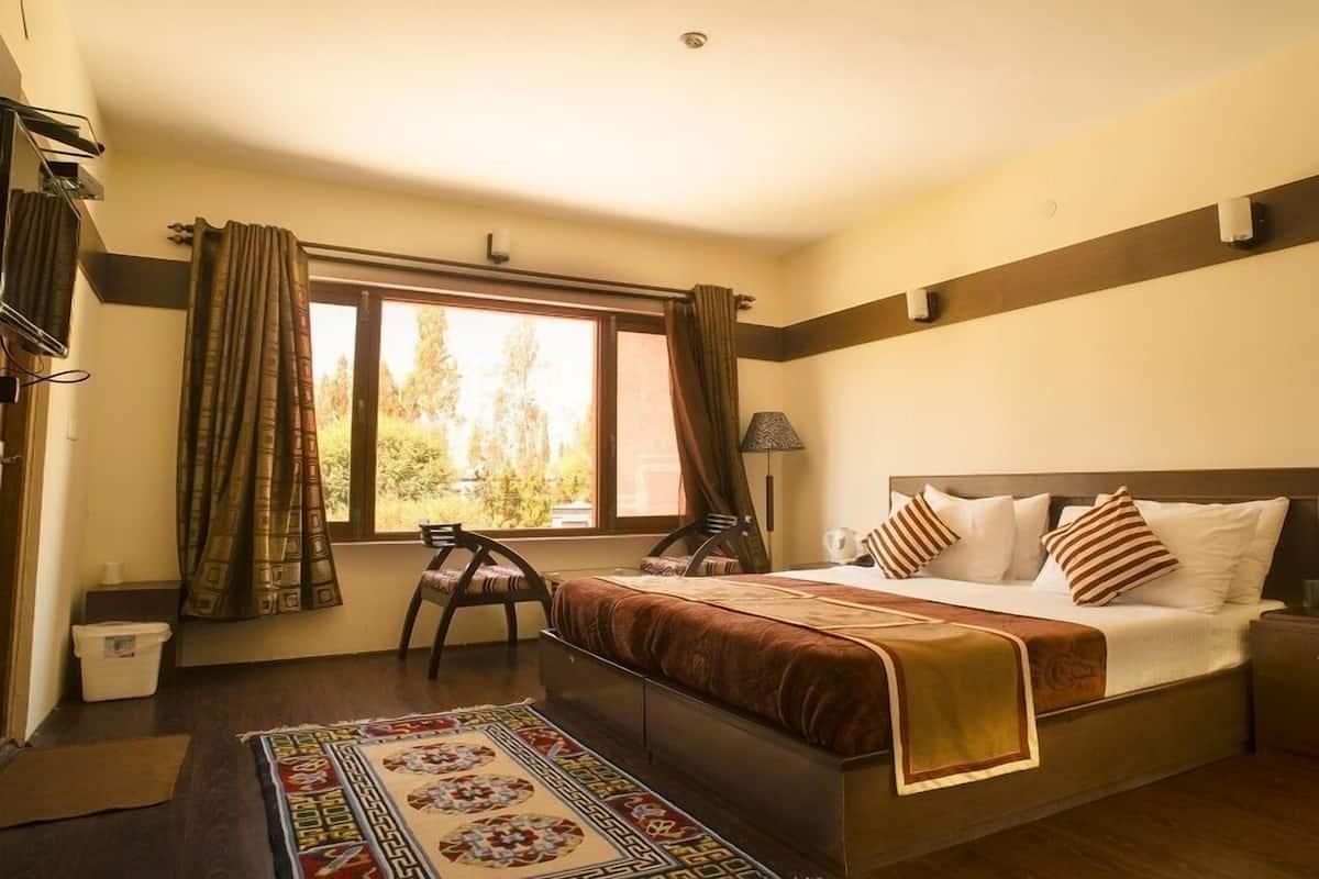 A bedroom with a bed, bedside table, lamp, chair, and a view of trees through the window.