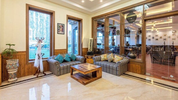 A spacious living room with a large window, a sofa set, a coffee table, and a display cabinet with various items. - Ladakh Himalayan Retreat (Leh)