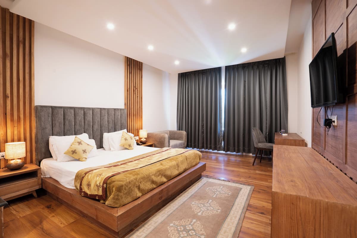 A modern bedroom with a large bed, wooden headboard, bedside tables, a flat-screen TV, and a large window with curtains.