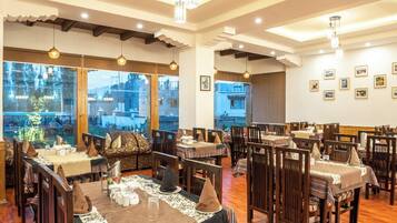 A dining area with multiple tables and chairs, large windows with a view, and pendant lighting.
