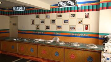Un área de bufé con una larga mesa de servicio, múltiples estaciones de comida y una pared decorada con fotografías enmarcadas.