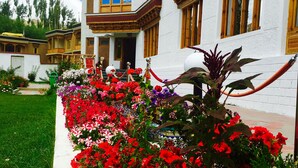 A building with traditional architecture, a well-maintained garden with colorful flowers, and a clear sky. - Ladakh Himalayan Retreat (Leh)