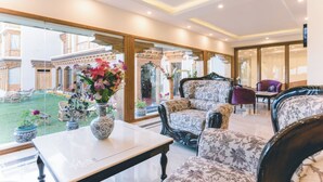 A spacious living area with a large window, a table with a vase of flowers, and a seating area with patterned sofas and armchairs. - Ladakh Himalayan Retreat (Leh)