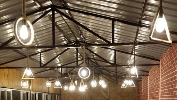 A communal dining area with people eating, a long table with food and dishes, and hanging pendant lights. - Camp Nirmit By Royal Collection (Dhari)