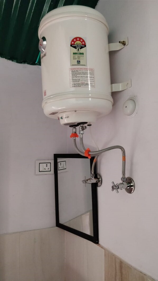 A white water heater mounted on a wall with a power savings guide sticker, connected to a wall-mounted faucet with a black frame.