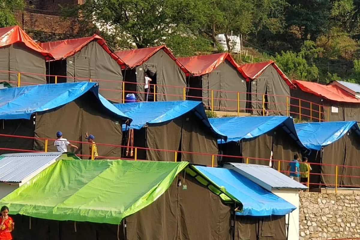 A row of tents with red roofs and blue tarps, some with people visible inside.