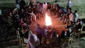 A group of people seated around a campfire in an outdoor setting. - Camp Nirmit By Royal Collection (Dhari)