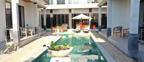 Un área de piscina con una zona de estar, una planta en maceta y una parrilla.