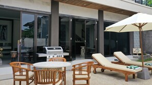 An outdoor patio with a grill, lounge chairs, and a table. - Villa Viking (Jimbaran)