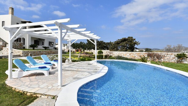 Une piscine dotée de chaises longues et d’une pergola, entourée d’un mur de pierre et de verdure.