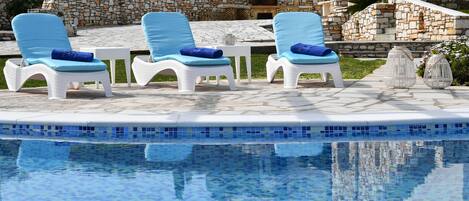 A poolside area with lounge chairs and a stone wall in the background.