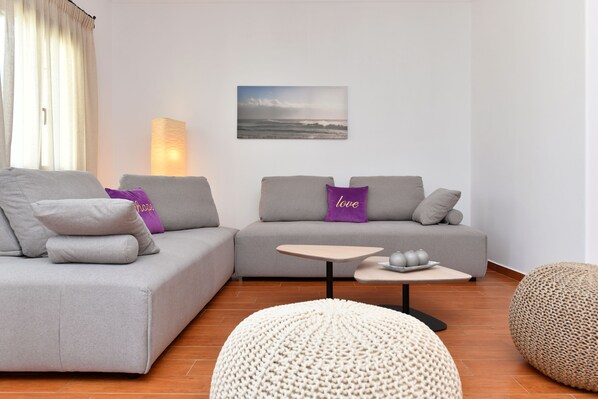 A modern living room with a grey sofa, a small round table, and a knitted pouf. - Villa Trifylia (Paros)