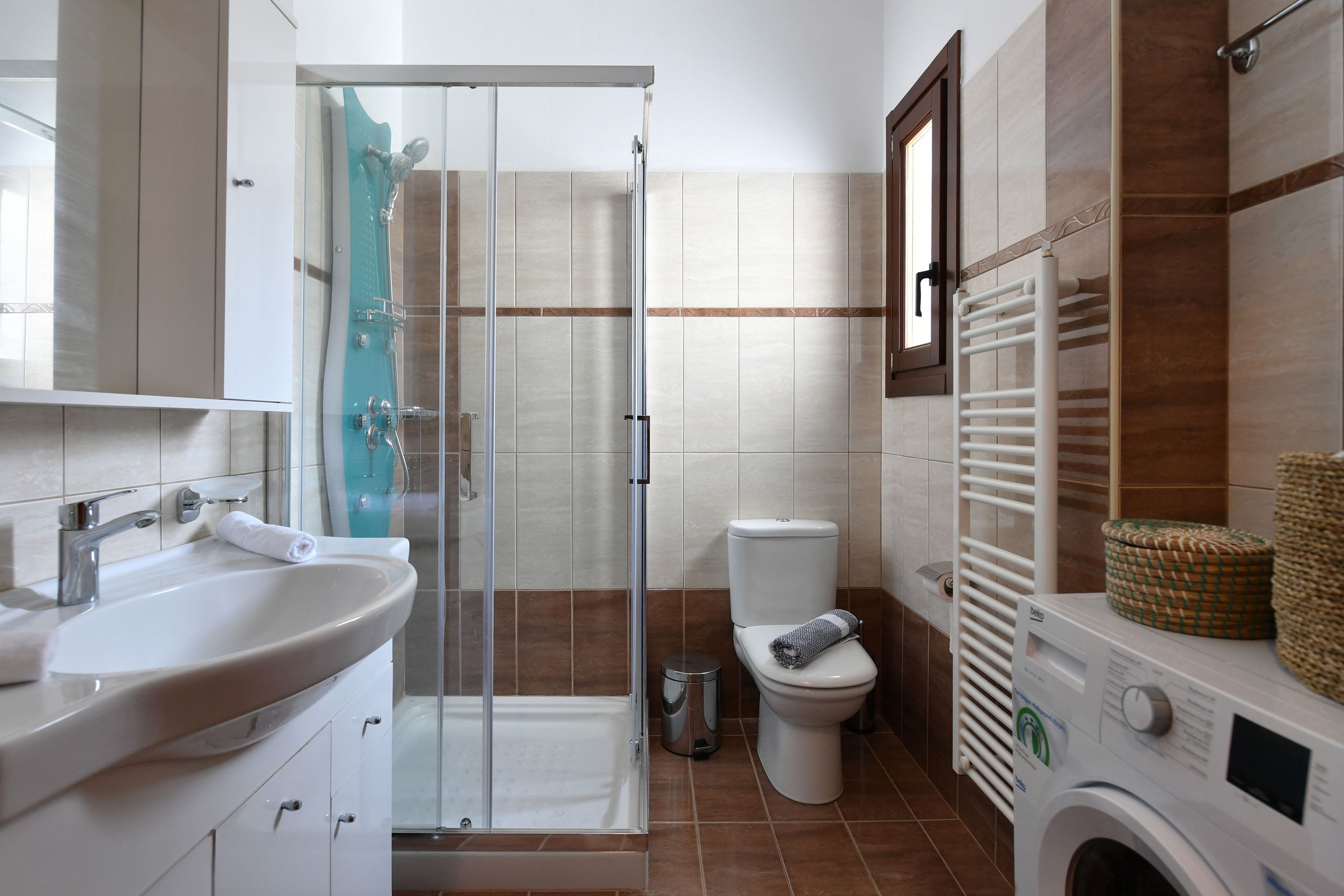 A bathroom with a glass-enclosed shower, a toilet, a sink, and a washing machine.