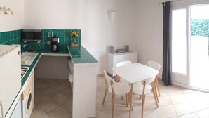 A compact kitchen with a microwave, coffee maker, and a small dining table with chairs. There is a sliding glass door leading to an outdoor area. - Villa STELLA D ORO, F2 * (Porto-Vecchio)