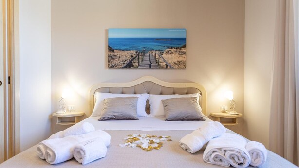A neatly made bed with white linens, a painting of a beach scene above it, and two bedside tables with lamps. - Domus Japigia (Ugento)