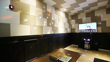 A modern room with a checkered wall pattern, a flat-screen TV, a console table with a book and a calculator, and a ceiling with recessed lighting.