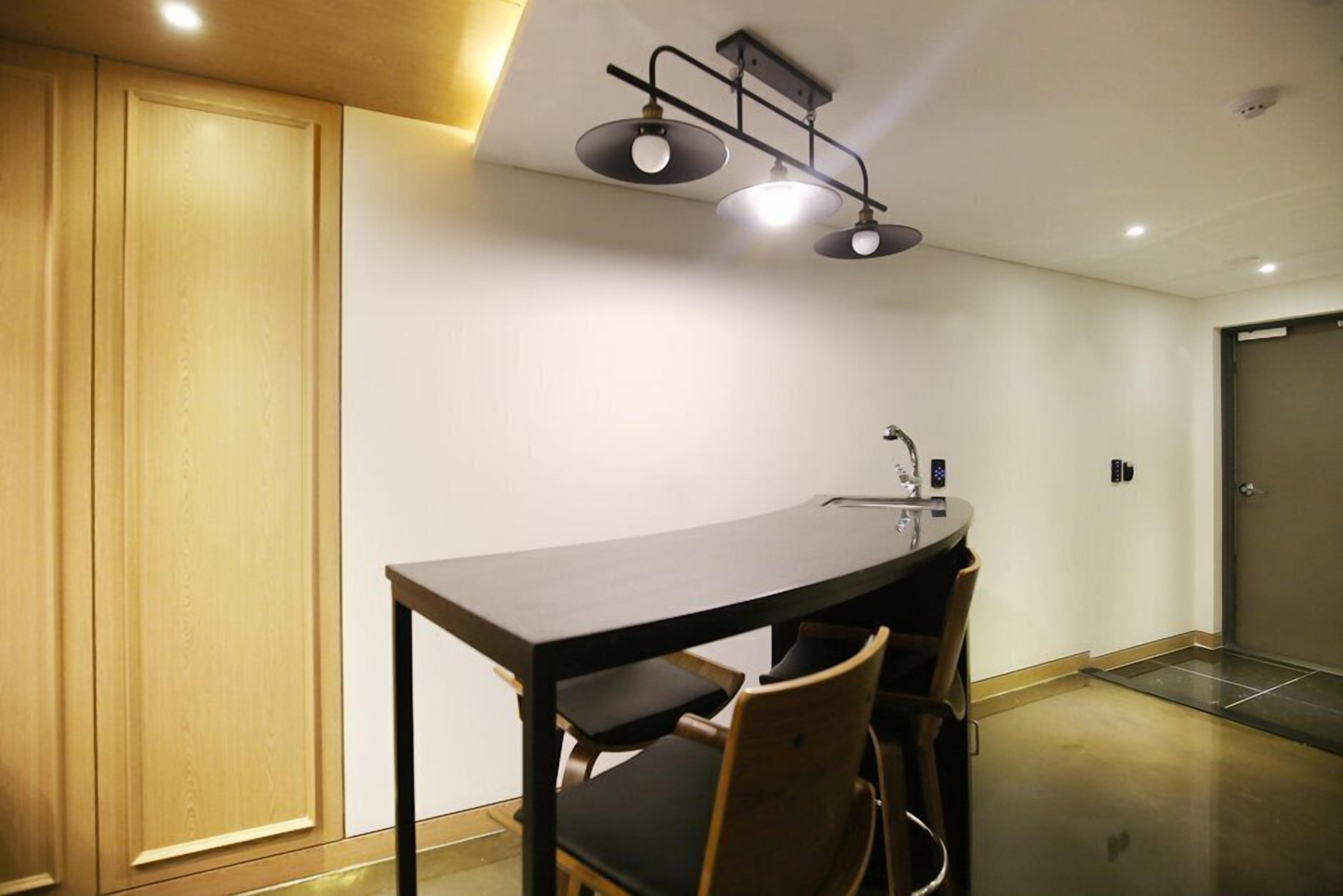 A small, modern kitchen with a dark wooden table and chairs, a built-in oven, and a ceiling light fixture.