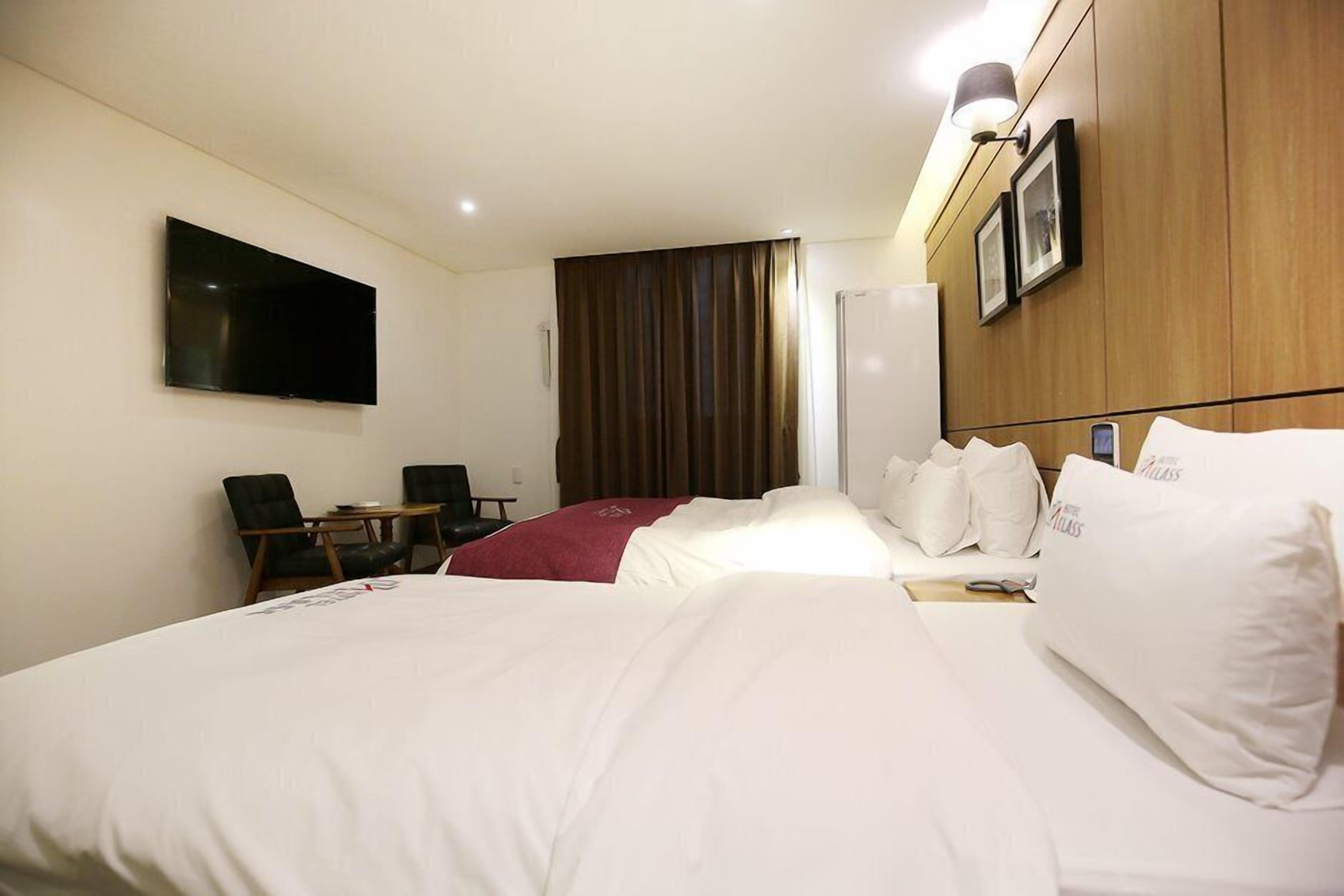 Habitación de hotel con dos camas, un televisor montado en la pared, un escritorio con silla y un armario.