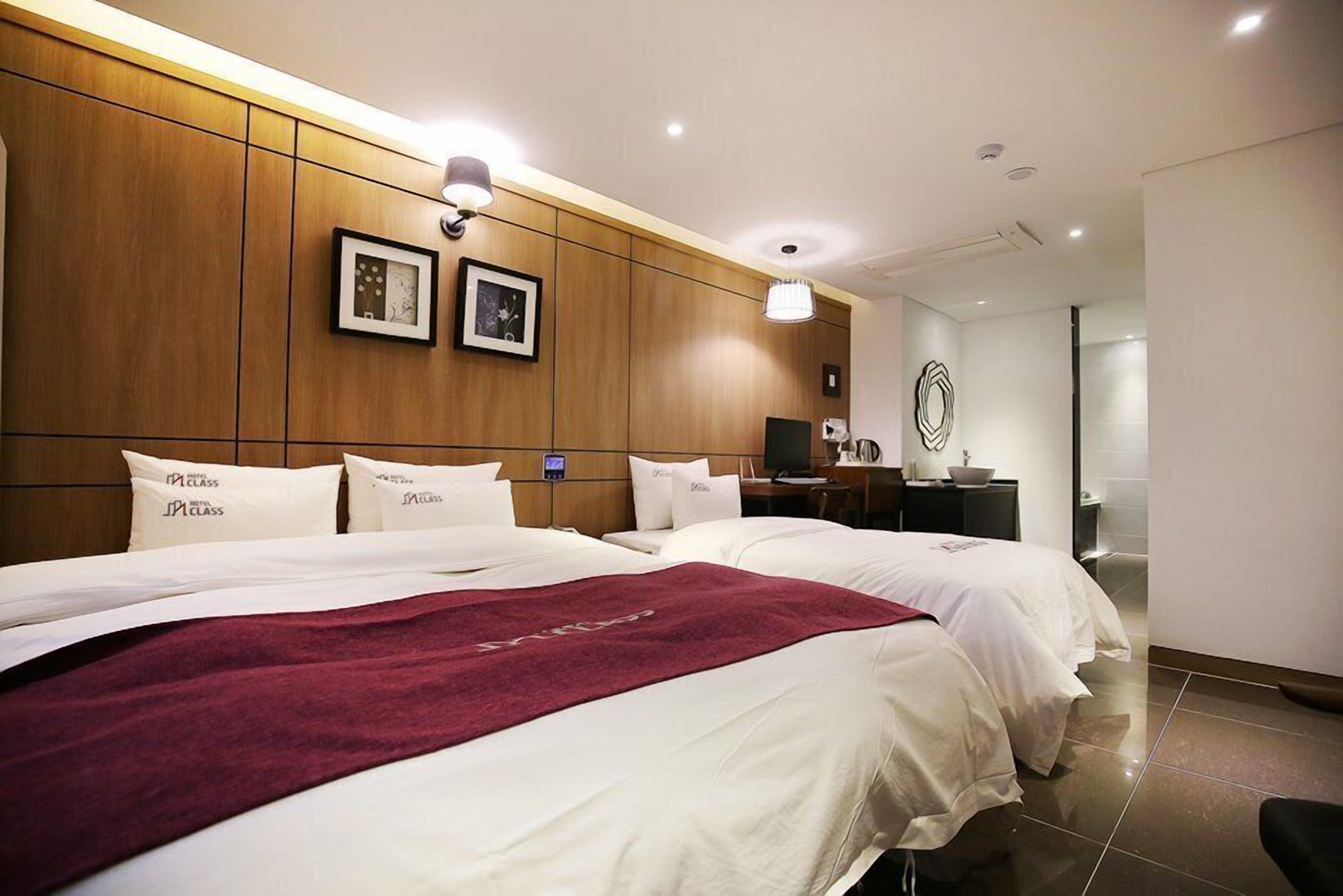 A hotel room with two beds, wooden paneling, a desk, and a bathroom visible through an open door.