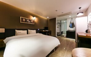 A modern hotel room with a large bed, a desk, and a bathroom visible through an open door.