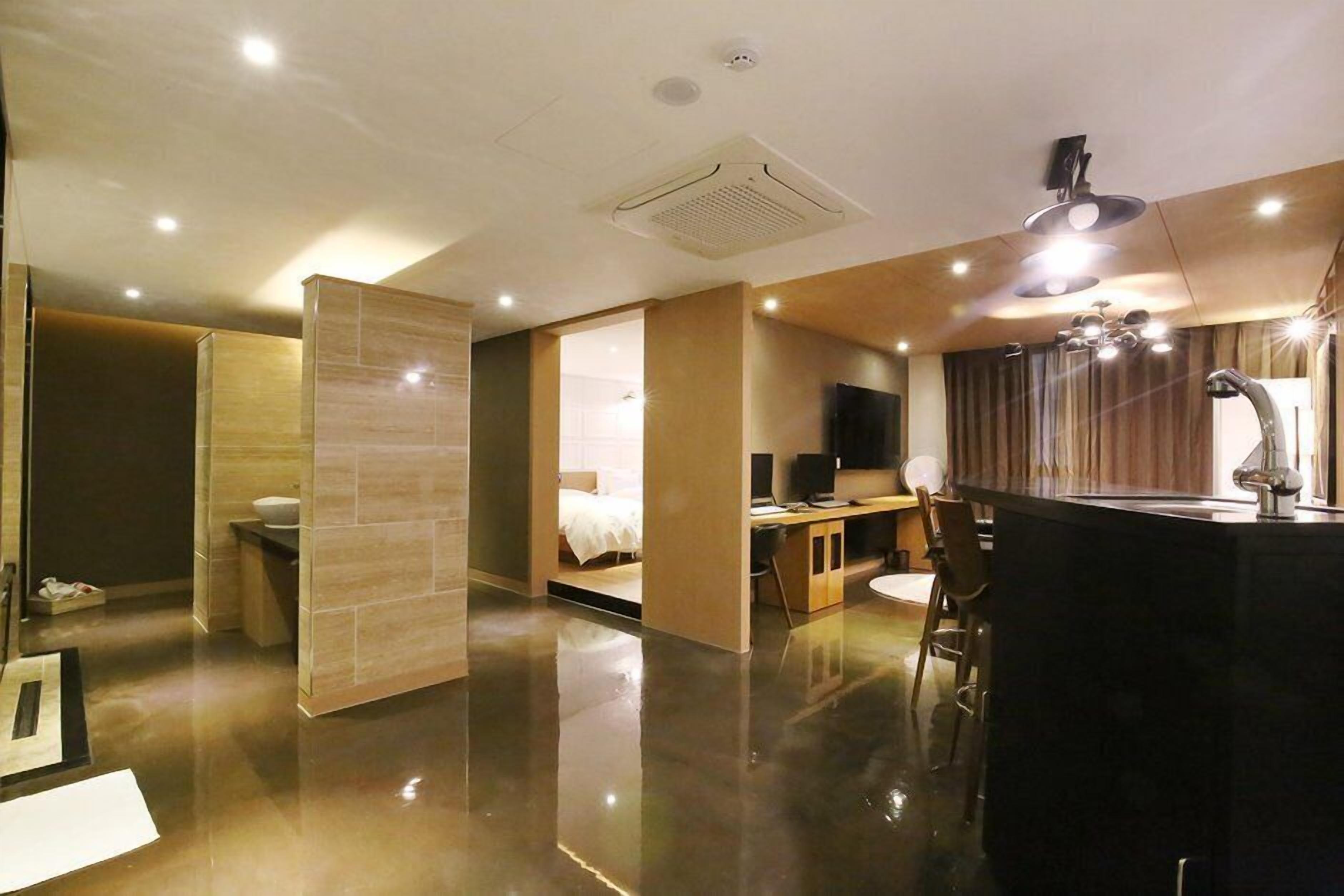A modern hotel room with a large bed, a desk with a computer, a bathroom, and a kitchen area.