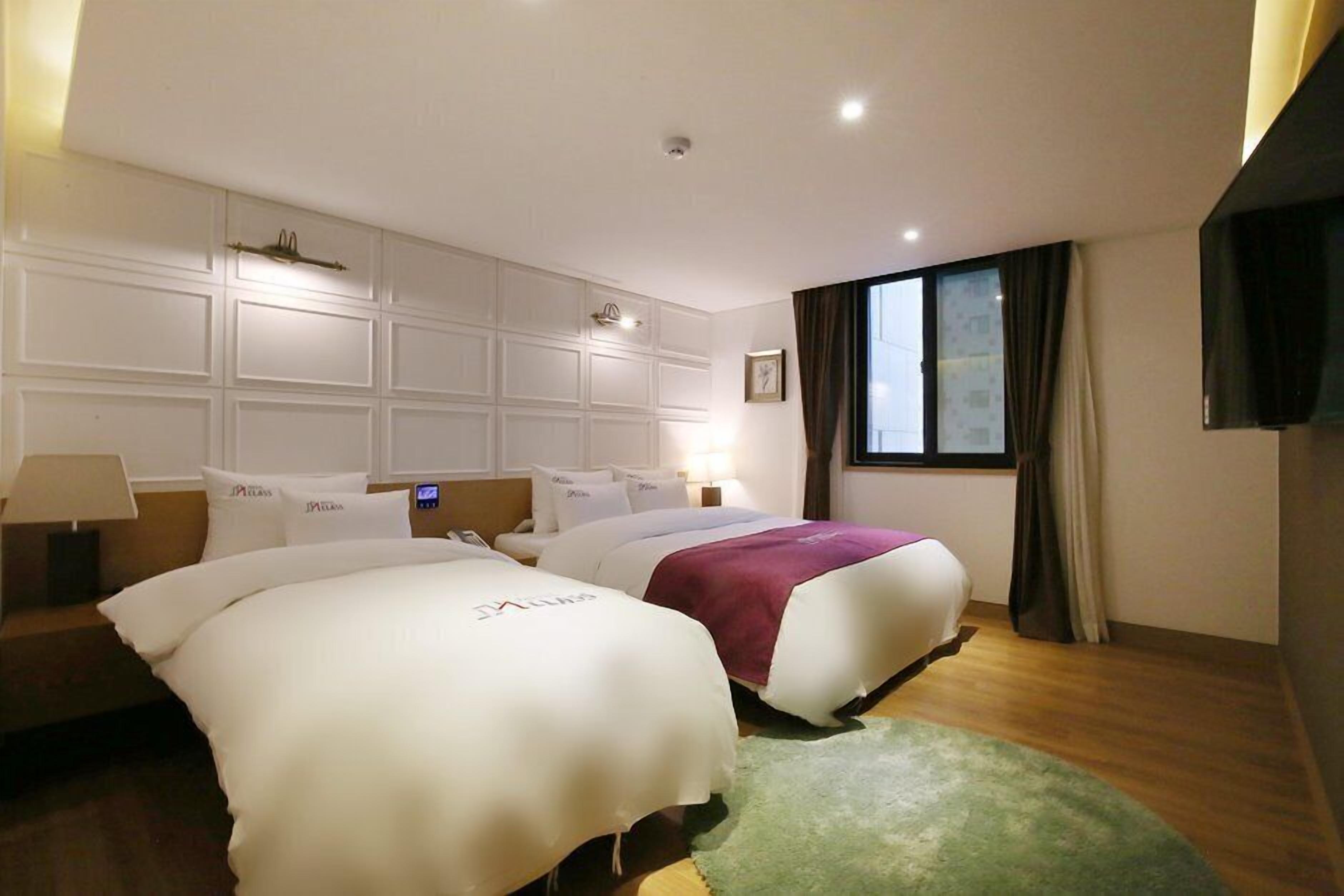 A hotel room with two beds, a large window, and a flat-screen TV.
