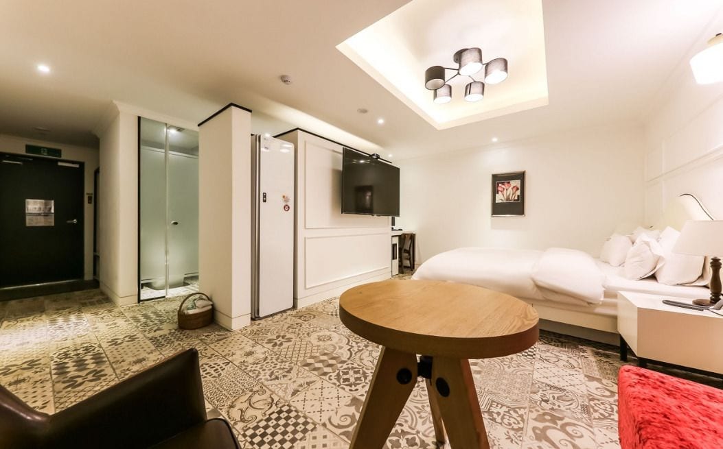 Habitació d'hotel moderna amb un sofà, una taula rodona de fusta, un televisor fixat a la paret i un paviment amb dibuixos.