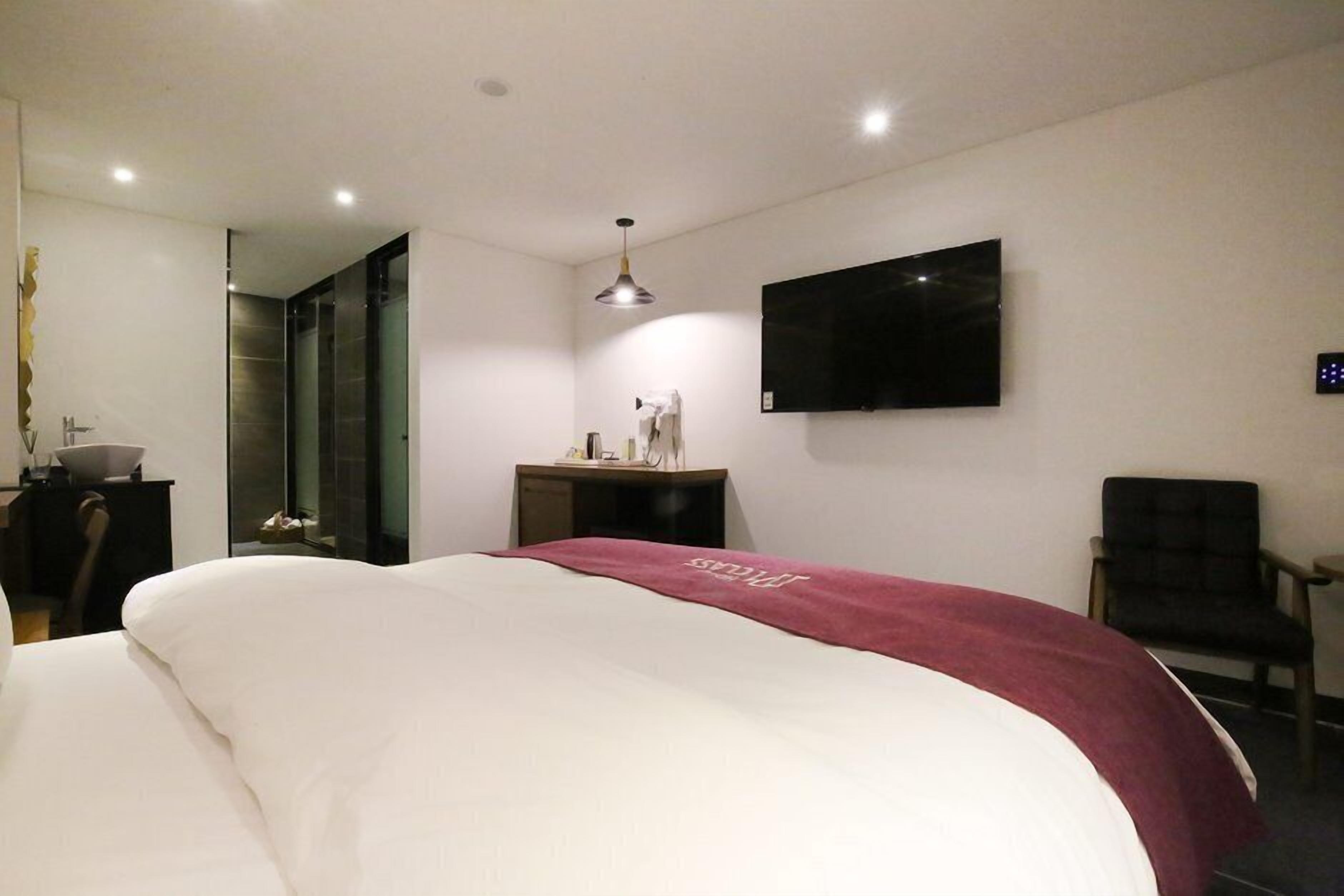 Una habitación de hotel moderna con una cama grande, un escritorio, una silla, un televisor montado en la pared y un espejo.