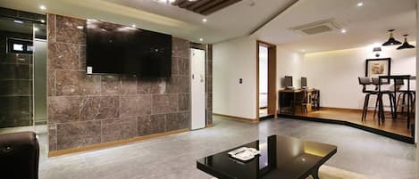 A modern living room with a large flat-screen TV, a black coffee table, and a dining area with chairs and a table.