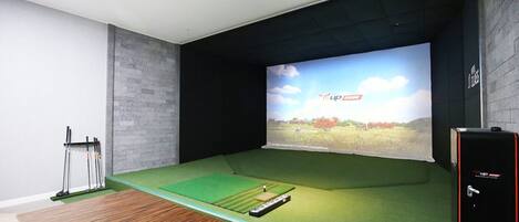 Una habitación con una pantalla grande que muestra un campo de golf, un proyector y un carrito de golf.