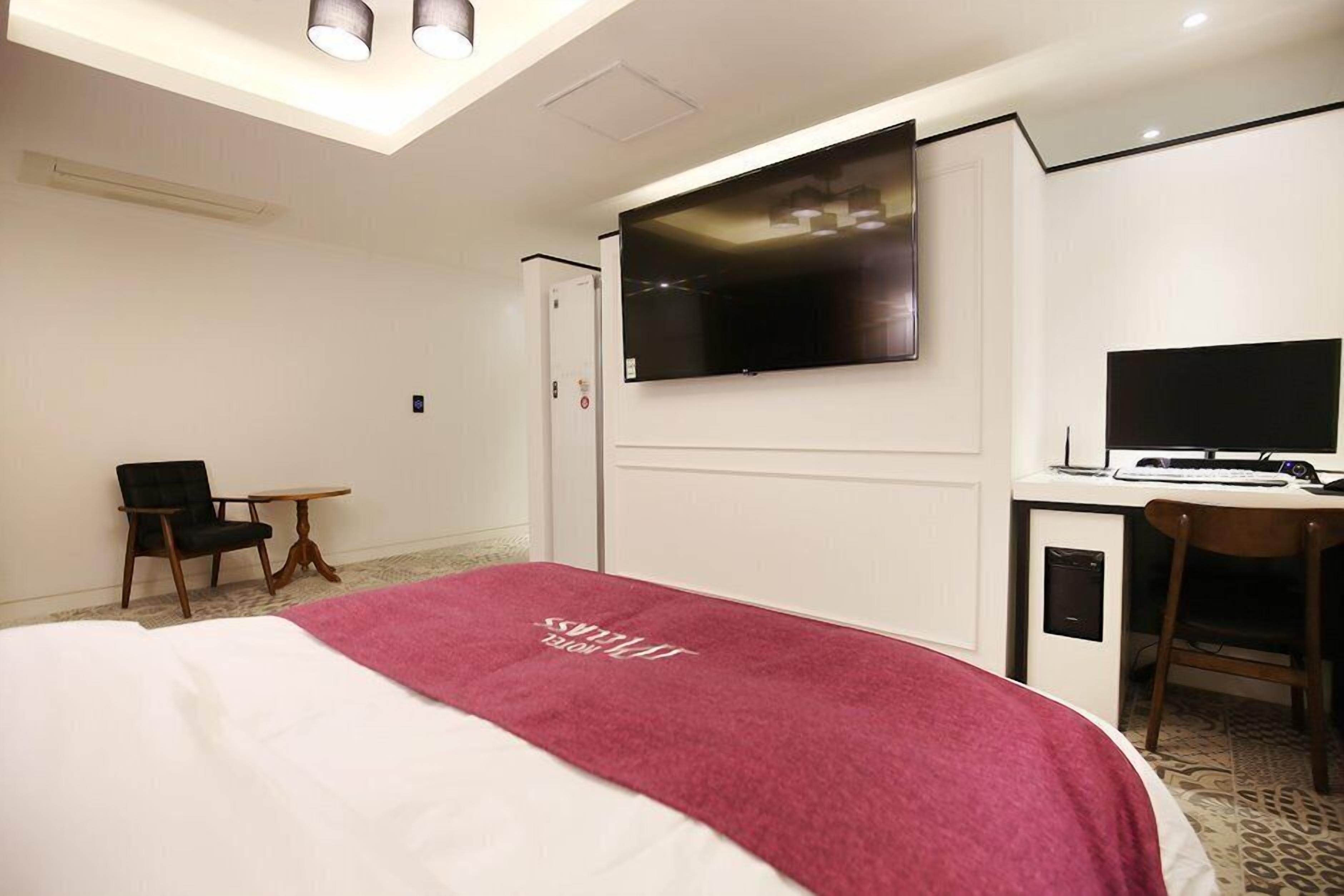 Ein Hotelzimmer mit Bett, Schreibtisch mit Computer, Stuhl, Wandfernseher und einem kleinen Tisch.