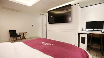 Ein Hotelzimmer mit Bett, Schreibtisch mit Computer, Stuhl, Wandfernseher und einem kleinen Tisch.