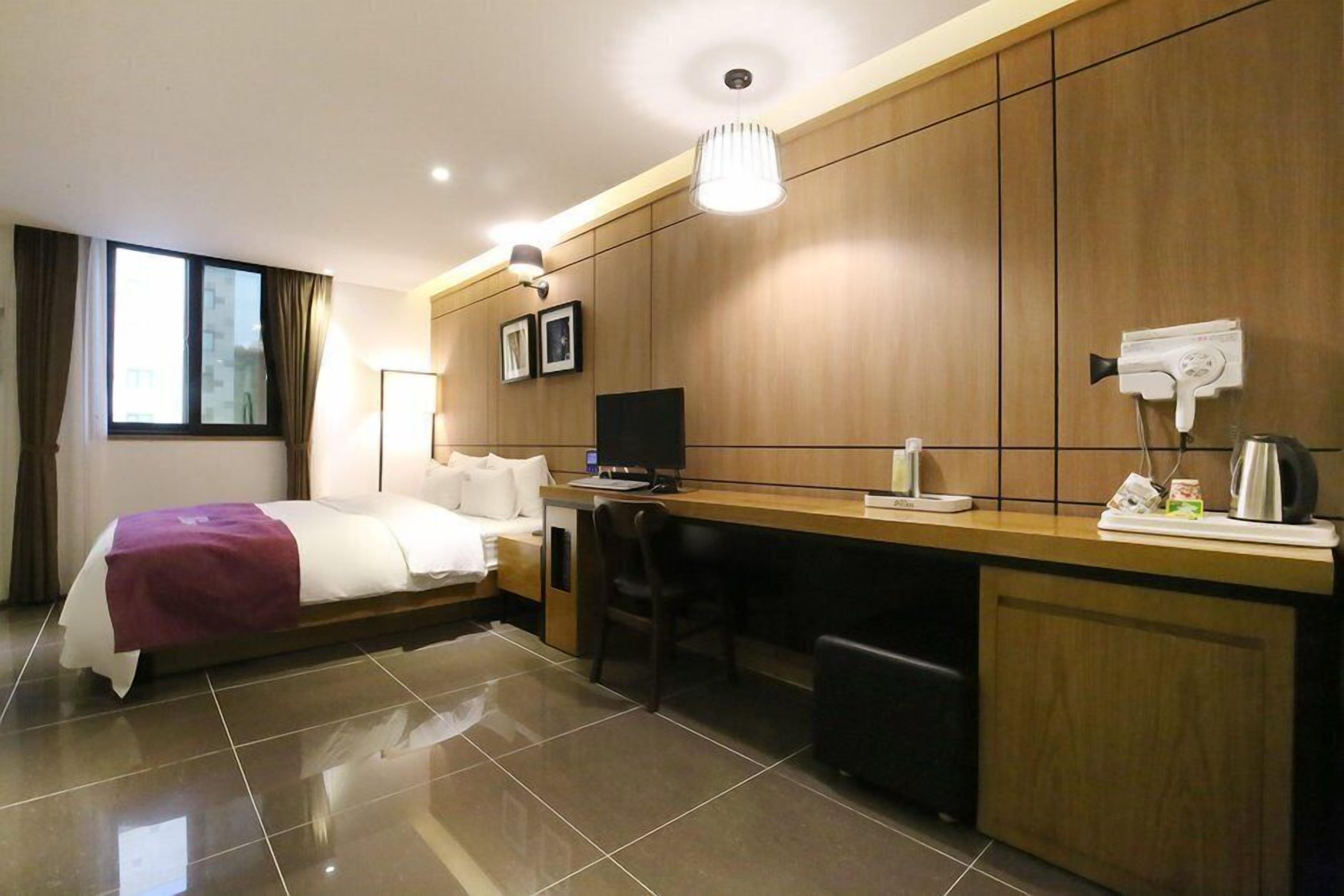 A hotel room with a bed, desk, chair, and a TV.