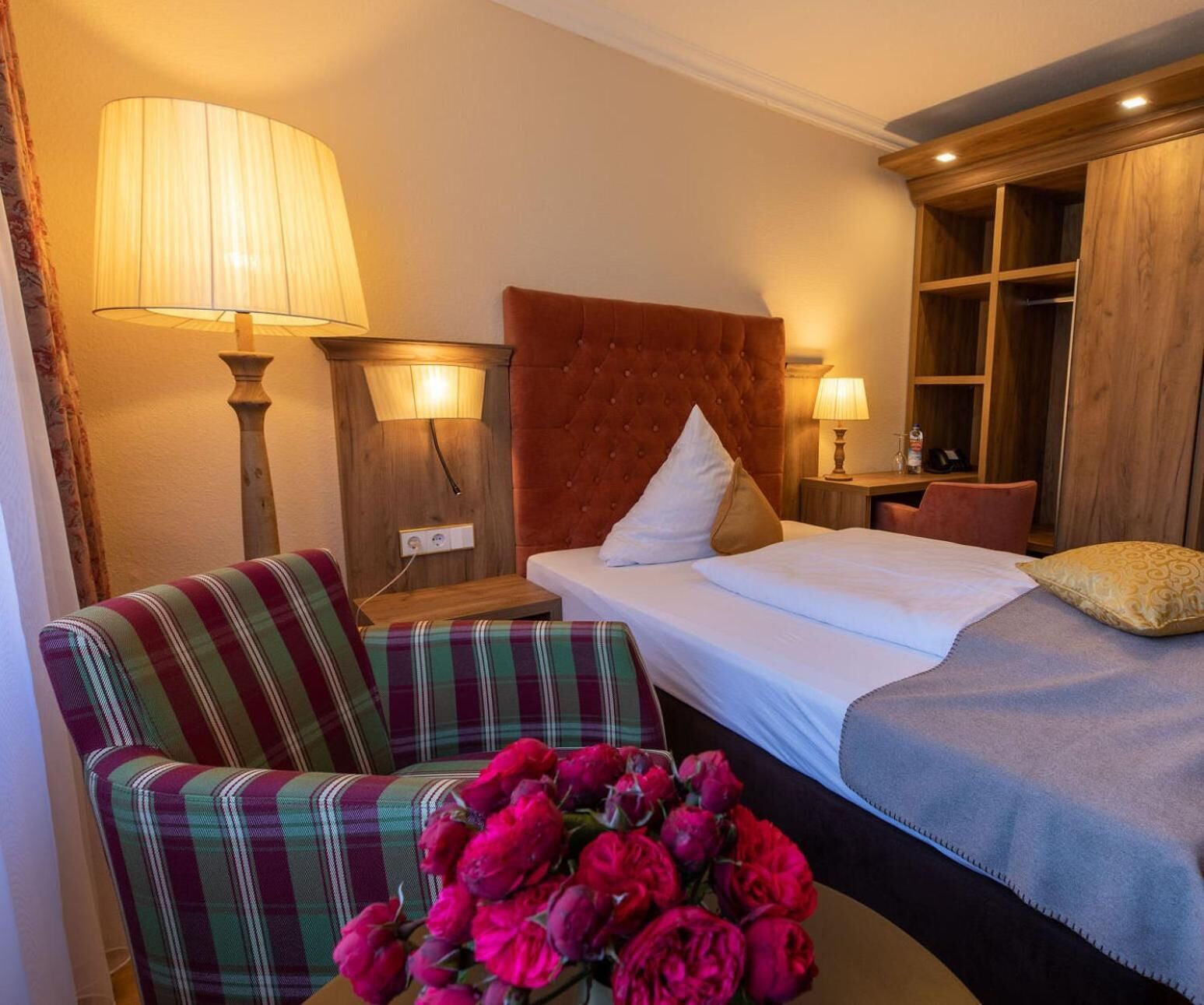 A hotel room with a bed, a chair, a nightstand, a lamp, and a window.