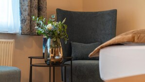 Quarto moderno com poltrona cinza, uma pequena mesa com um vaso de flores e uma janela com cortinas.