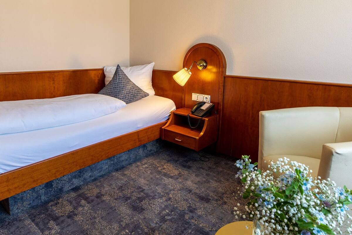 Une chambre d’hôtel avec un lit simple, une table de chevet avec une lampe, un téléphone et une chaise.