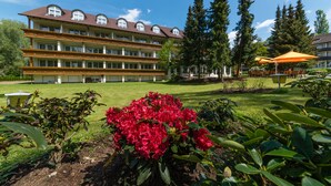 Hotel de vários andares com área de jardim, flores vermelhas e plantas verdes.