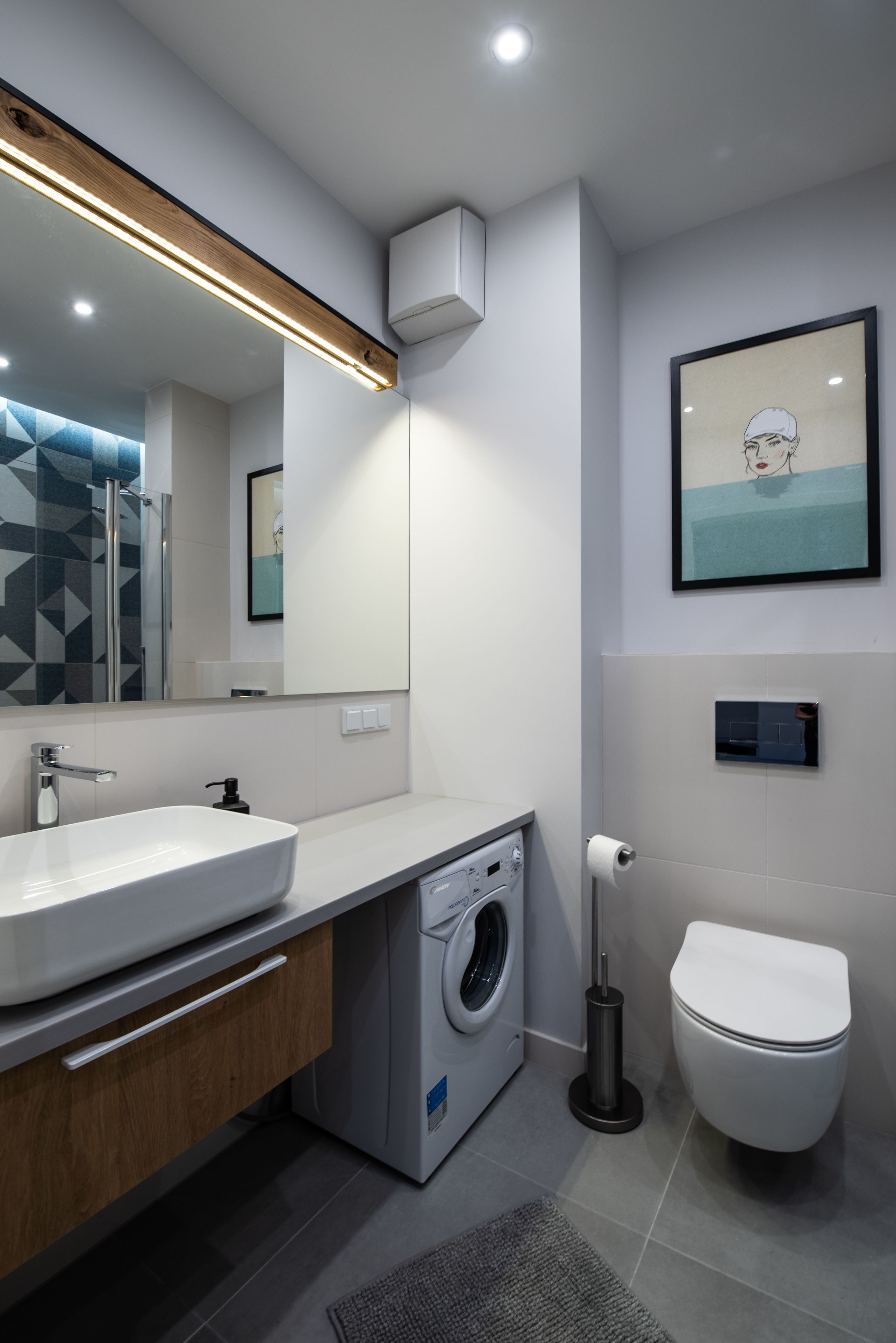 A modern bathroom with a large sink, a washing machine, a toilet, and a mirror with a geometric-patterned shower curtain.