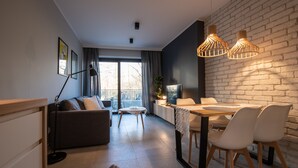 A modern living room with a sofa, a dining table with chairs, a TV, and a large window with curtains. - City Lights Apartments - Rakowicka 15 (Kraków)