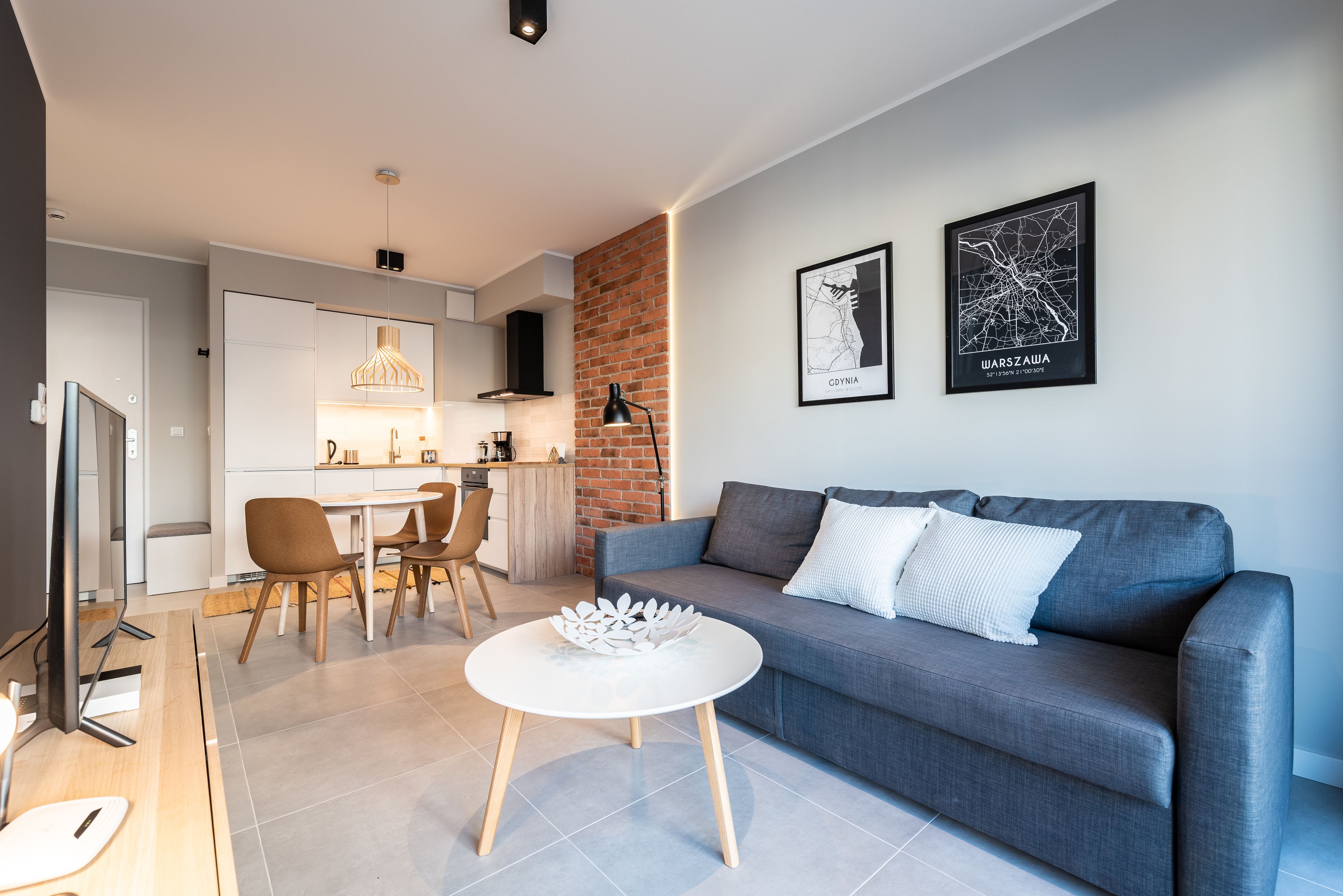 Una sala de estar moderna con un sofá gris, una mesa de centro blanca y un comedor con una mesa y sillas de madera.