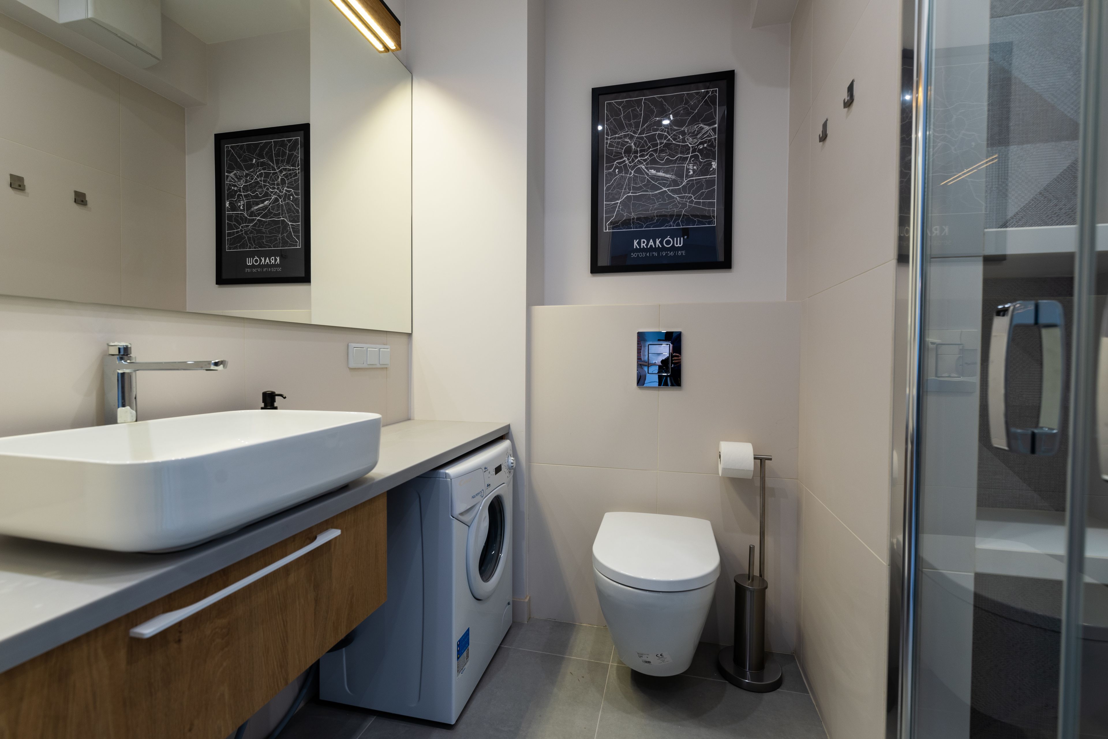 Un baño moderno con un lavamanos grande, una lavadora, un inodoro y mapas enmarcados en las paredes.