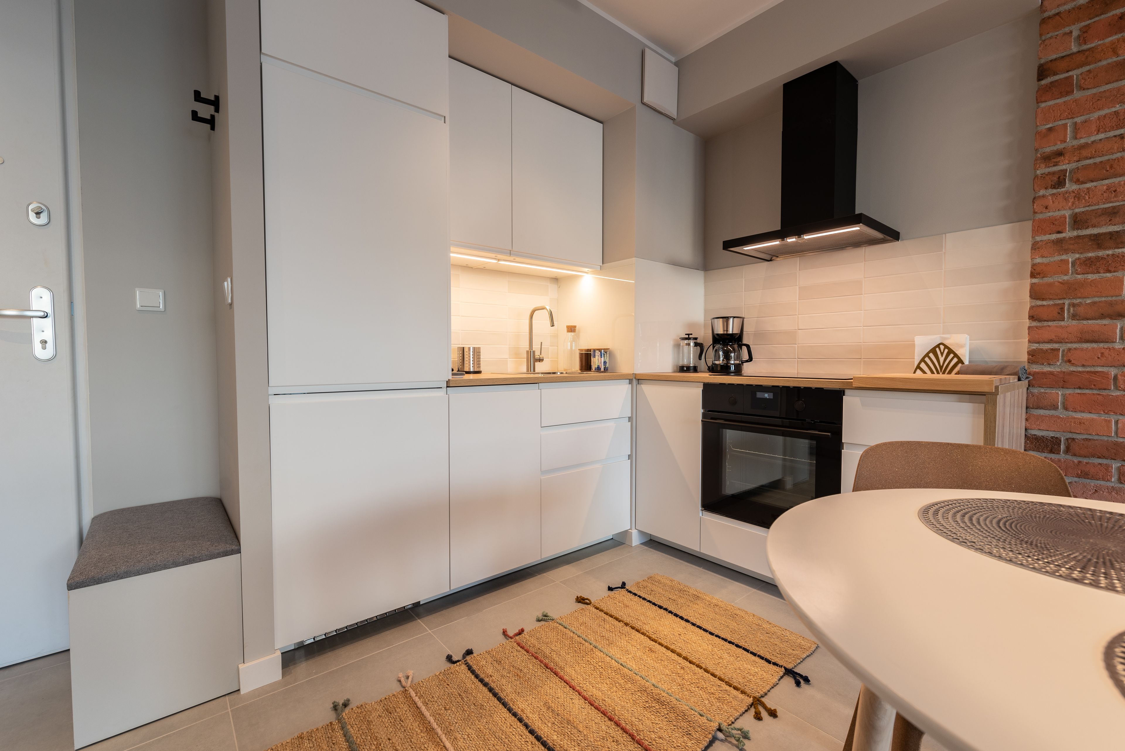 Une cuisine moderne avec des armoires blanches, une hotte noire et un mur d’accent en briques.