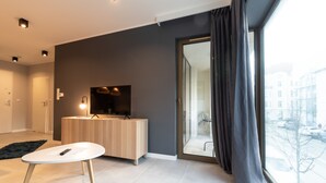 A modern living room with a flat-screen TV, a wooden cabinet, and a large window with curtains. - City Lights Apartments - Rakowicka 15 (Kraków)
