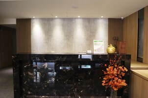 A reception desk with a black marble top, a wooden panel wall, and a vase with orange flowers.