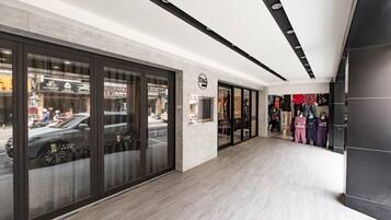 A modern interior with a clean, minimalist design, featuring a spacious corridor, glass storefronts, and a display of clothing racks.