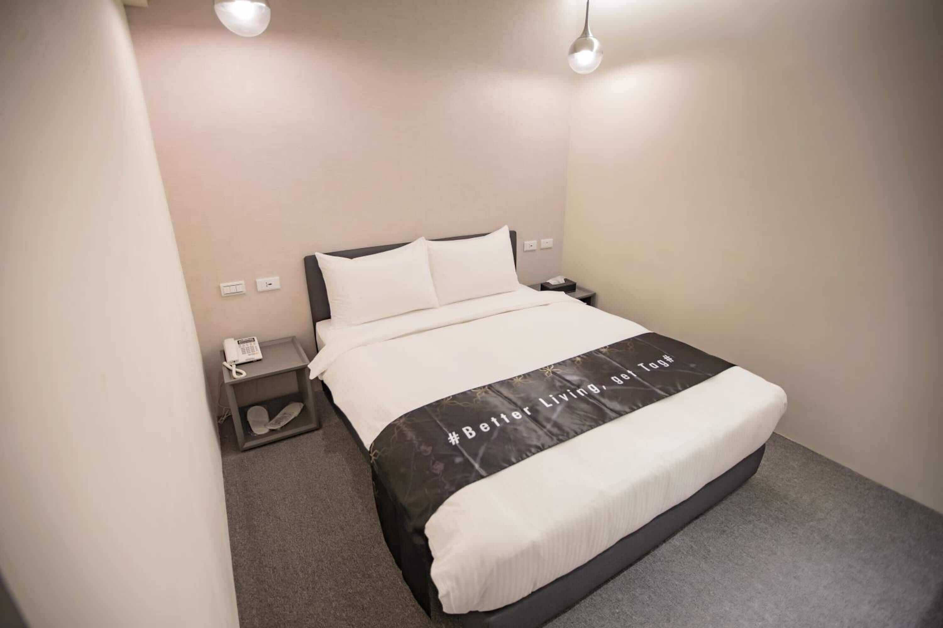 A hotel room with a bed, a bedside table with a phone, and a wall socket.