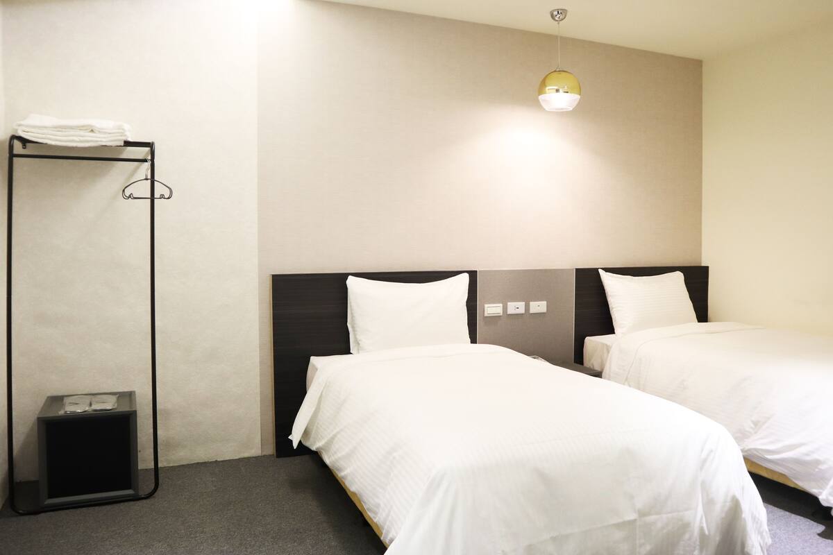 A hotel room with two beds, a wardrobe, and a small trash bin.