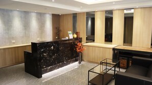 A modern reception area with a marble reception desk, a glass coffee table, and a wooden accent wall. - Tag inn (Taoyuan City)