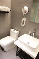 Un baño con inodoro, lavamanos y secador de pelo fijado a la pared.